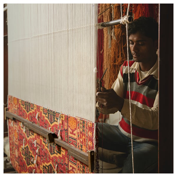 Person weaving colourful rug on loom.