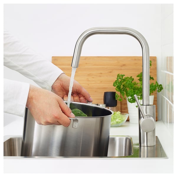 Person som tvättar gröna grönsaker under en modern, vattenbesparande köksblandare med hög pip.