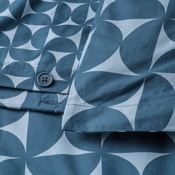 Närbild av en knapp på ett mönstrat påslakan. Blå geometriska former på ljust tyg.
