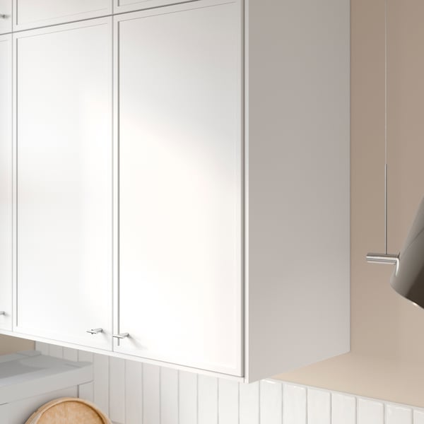 Vita köksskåp med tunna ramar, matt finish och synliga gångjärn. Överskåpet är stängt, vilket visar rena linjer och modern design.