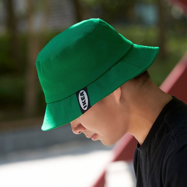 Person som bär en ljusgrön hatt med en svart logotyp på sidan, som troligen njuter av utomhusaktiviteter.