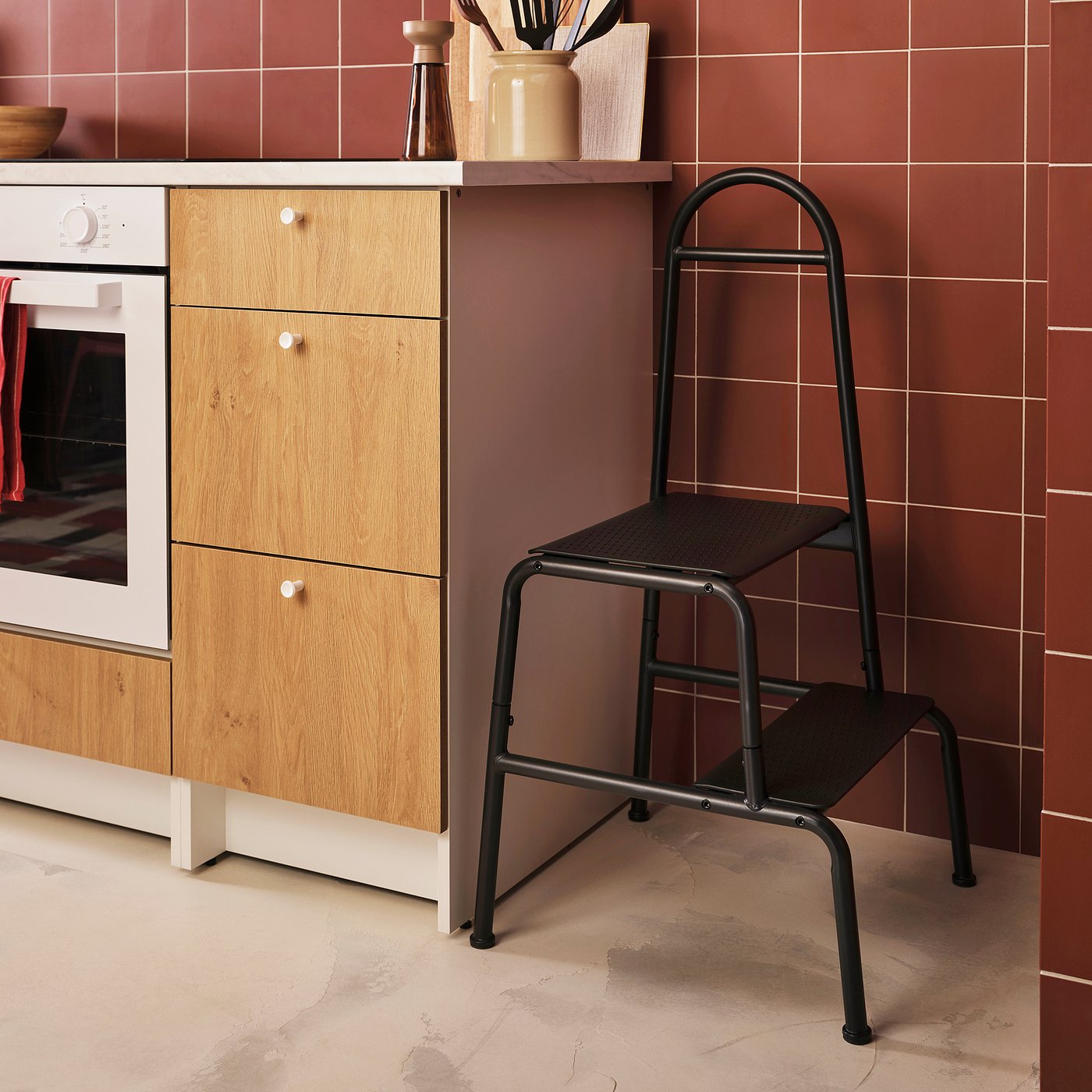 Kök med svart BÄSINGEN 2-stegs pall, mörkgrå metallram, träskåp och rött kakel.