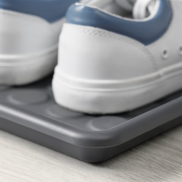 Närbild av en vit och blå sneaker som vilar på en grå skomatta av plast på ett trägolv.