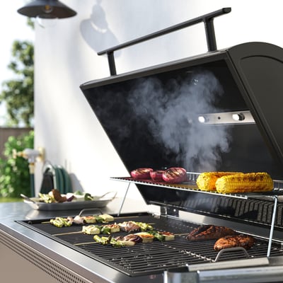 Svart utomhusgrill med flera matvaror som lagar mat. Inkludera justerbara fötter, en inbyggd termometer och ett värmeställ.