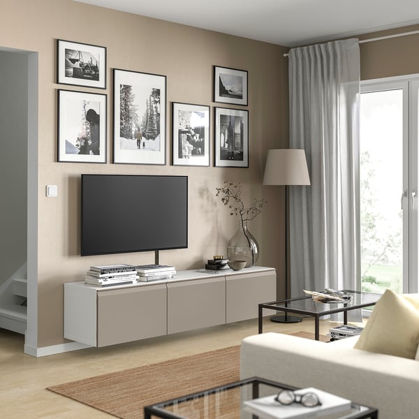 Modernt vardagsrum med tv-bänken BESTÅ, svart tv, grå gardiner, svartvita bilder, soffbord i glas, beige soffa.