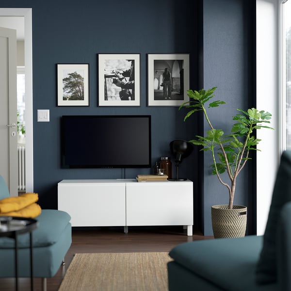 Modernt vardagsrum med tv-bänken BESTÅ, platt-tv, foton, inredning, grön växt, blå stolar och gul kudde.