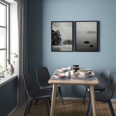 Modern matplats med blå stolar, träbord och två inramade svartvita naturkonsttryck på blå vägg.