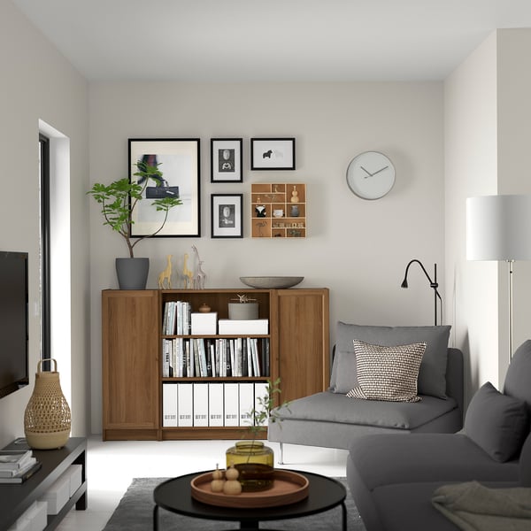 Valnöt BILLY bokhylla bredvid grå soffa med inredning, klocka ovanför, minimalistisk design.
