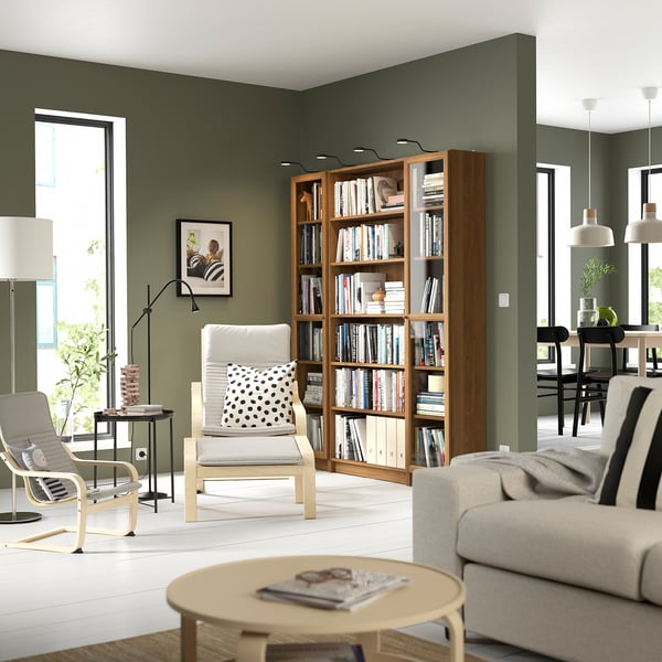 Bokhylla BILLY i trä med glasdörrar och böcker i mysigt grönt vardagsrum.