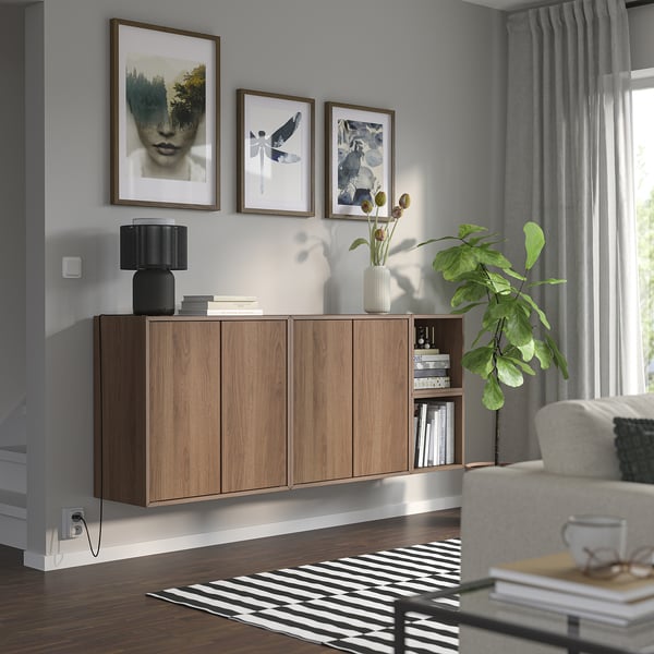 Modernt vardagsrum med vägghängda EKET-skåp, böcker och inredning. Konst, växter, gråa gardiner, randig matta.