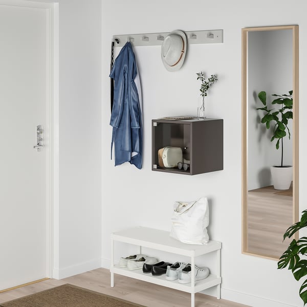 Minimalistisk entré med skohylla, klädkrokar, skåp, spegel och växt.
