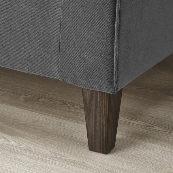 Soffa närbild: mörkgrå klädsel, avsmalnande ben i trä, polerat golv.