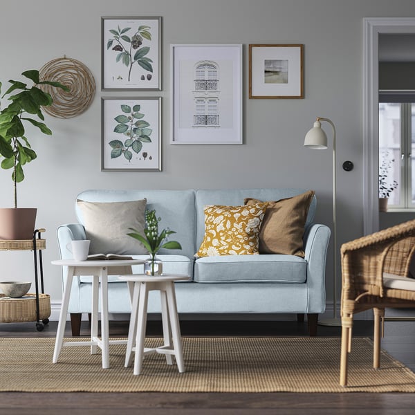 Modernt vardagsrum med blå soffa EKHOLMA, soffbord, växt och väggkonst.