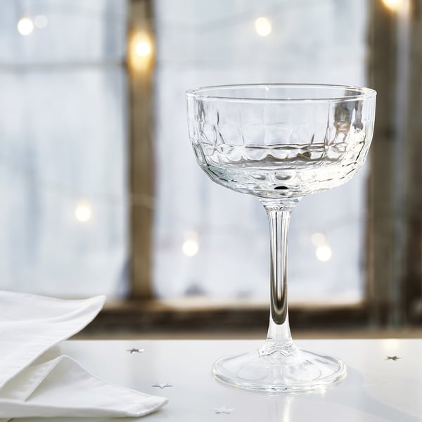 Klar, elegant champagnecoupé med intrikat design på en blank yta, bredvid prydligt vikta vita servetter.