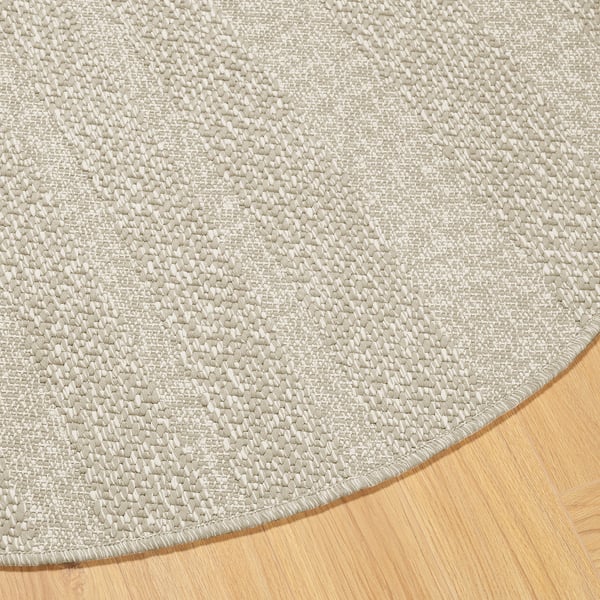 Rund matta med texturerat beige mönster på trägolv som framhäver dess intrikata väv och släta kanter.