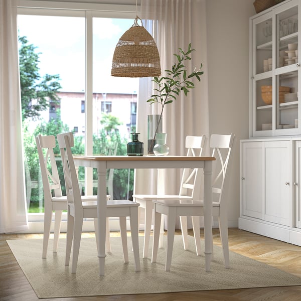 Beige matta passar under matbordet med 4 stolar, omgiven av vit inredning inklusive lampa, vaser och växt vid fönstret.