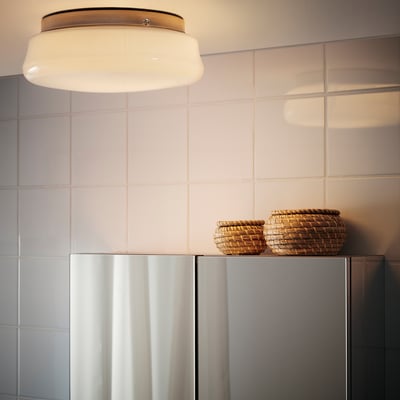Ett modernt badrum med en rund taklampa som ger diffust ljus, och två flätade korgar ovanpå ett skåp.