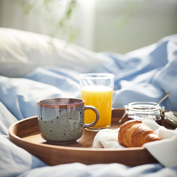 Frukostbricka med GLADELIG mugg, apelsinjuice, bakverk, sylt. Muggen är blå, stor, keramisk med prickig design.