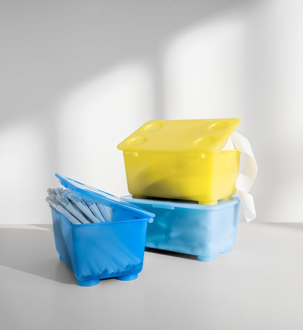 Två färgglada plastförvaringslådor; en blå, en gul, staplad med lock på och ett band fäst för bärning.