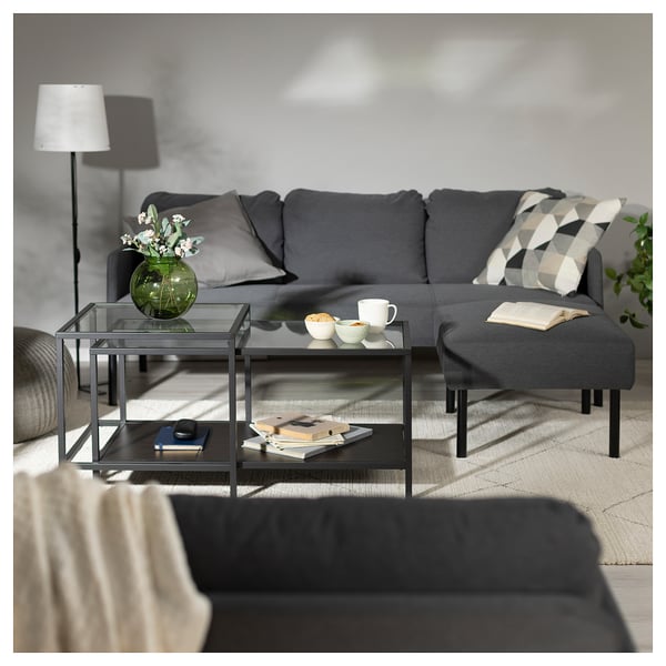 Modernt vardagsrum med grå GLOSTAD soffa, soffbord i glas och grå fotpall. Dekorativ kudde, lampa och vas med blommor.