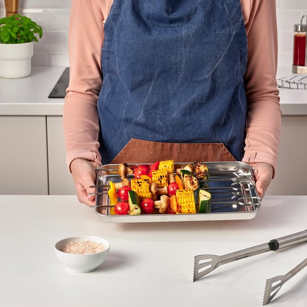 Person som håller en bricka i rostfritt stål fylld med färgglada grillade grönsaker och spett.