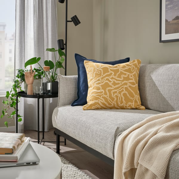 Minimalistiskt vardagsrum med grå soffa, senapsfärgad kudde, litet svart bord, vitt soffbord och stort fönster.