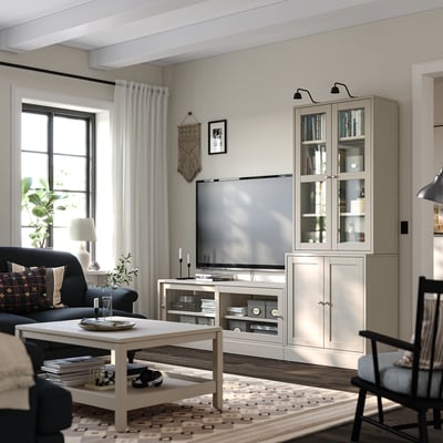 Modernt vardagsrum med tv-möbel i ljust trä, bokhylla och mörk soffa. Platt-tv, soffbord, gardiner och väggdekorationer.