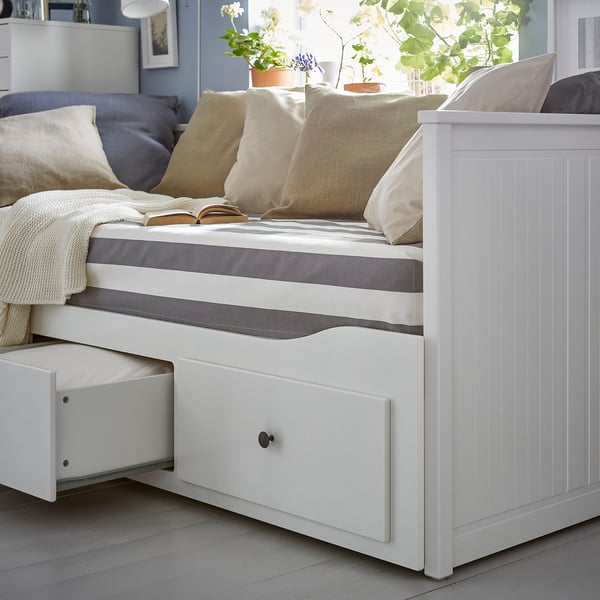 Vit HEMNES dagbädd med lådor, gräddvita kuddar, grå och vita sängkläder och växter.
