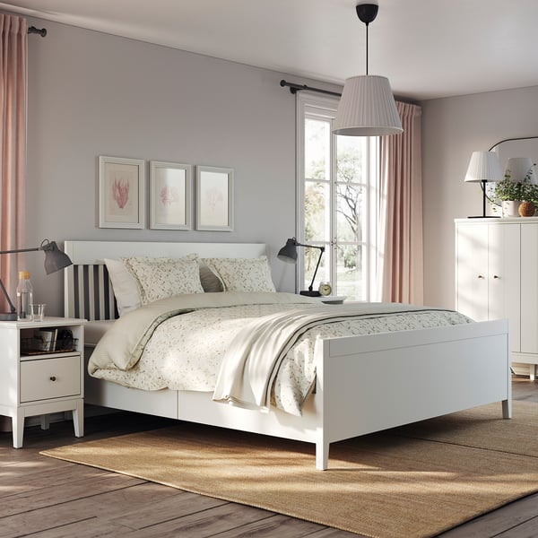 Modernt sovrum med vit säng, mjukstängande lådor, mönstrade sängkläder, svarta lampor, neutrala gardiner, botaniska tryck, mysig matta.
