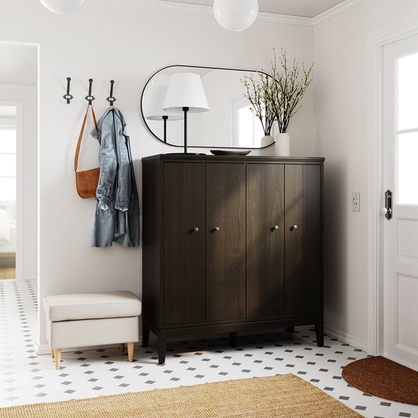 Elegant entré med IDANÄS skåp i mörkt trä, spegel, krokar, lampa, vas, pall och geometrisk matta.