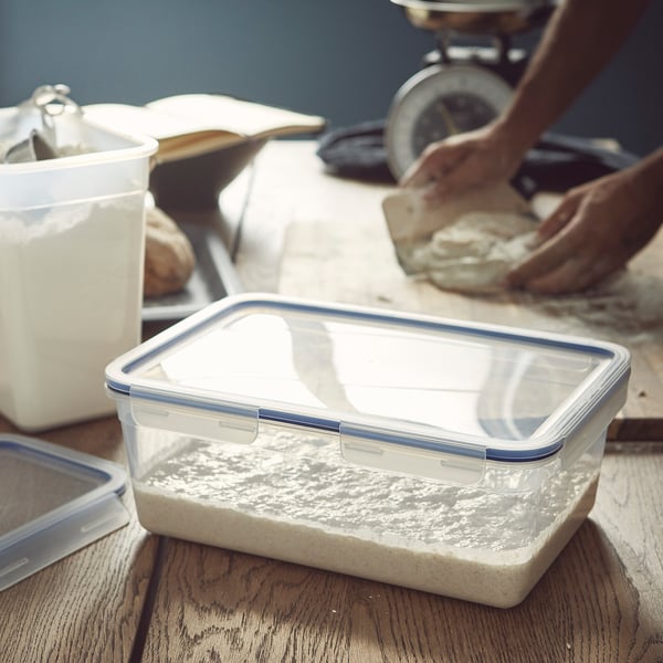 Person som förbereder deg bredvid en tom, klar, läckagesäker matbehållare på ett träbord.