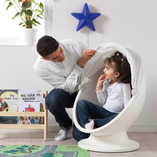 Mannen lutar sig mot ikea stolen där flickan sitter, böcker bredvid.
