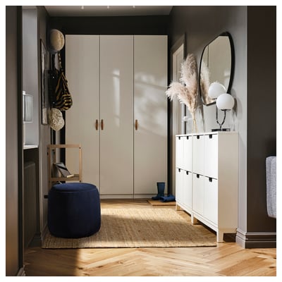 Modern entré med benvit garderob, vitt skoskåp, blå JÄRRESTAD puff, trästol och dekorerad hylla.