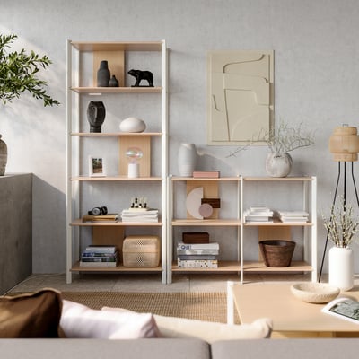 Modernt, ljusbeige vardagsrum med ljusa trähyllor fyllda med böcker och inredning. Abstrakt konst och naturliga element.