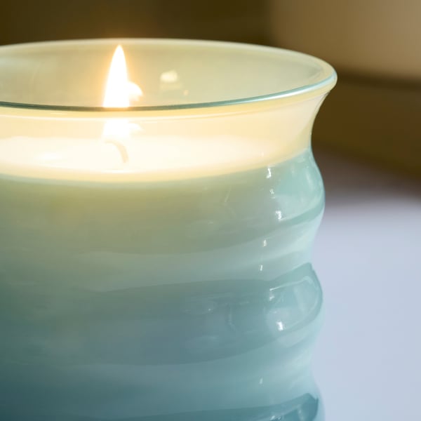 Cylindriskt glasljus med vågig textur, tänt inuti ljuset, avger ett mjukt sken.