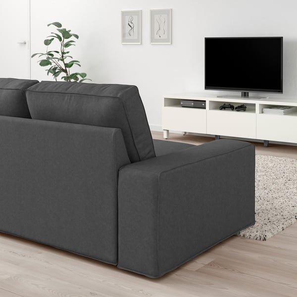 Grå KIVIK soffa, tv, växt i modernt vardagsrum. Trägolv, vita väggar, abstrakt konst. Mysigt, minimalistiskt.