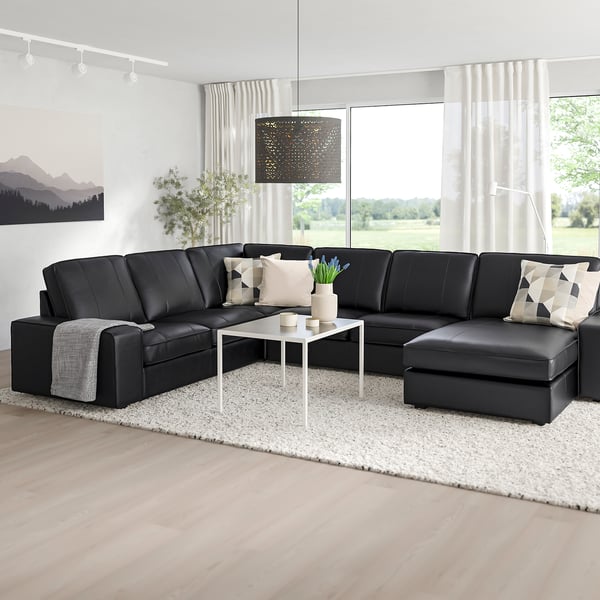 Elton svart KIVIK sektion, läder och tygblandning, stora och bekväma, breda armstöd, placerade framför höga fönster, kompletterade med vit inredning.