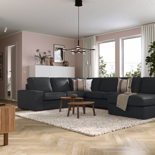 Modernt vardagsrum med KIVIK mörkgrå sektionssoffa, träbord, rosa väggar, stora fönster och vita gardiner.