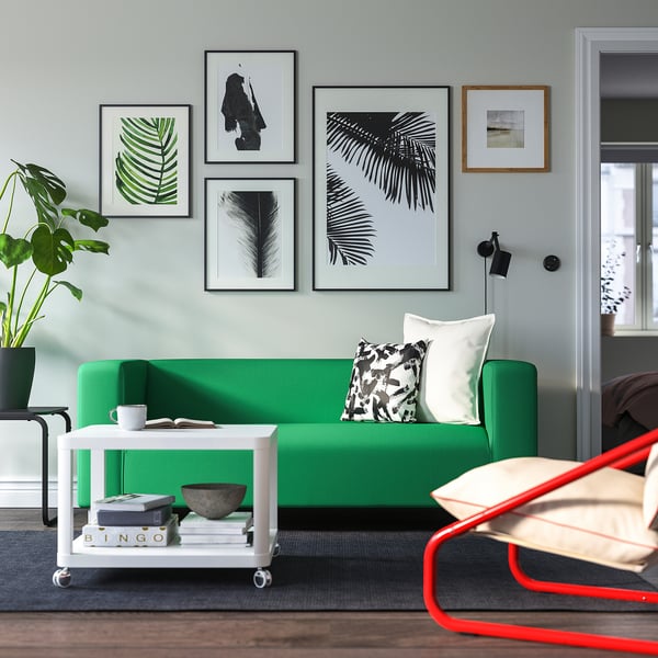 Ljust vardagsrum med grön soffa KLIPPAN, trendiga prints, vitt kartellbord och röd stol.