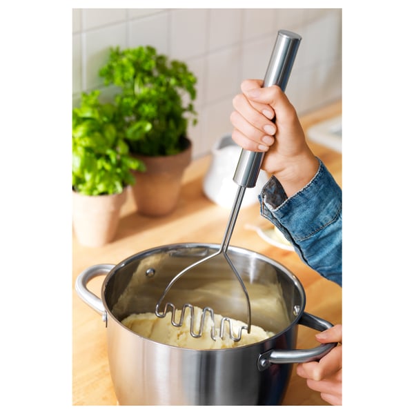 Person som mosar potatisar med hjälp av en metallmosare. Det långa handtaget gör att du når djupa krukor.