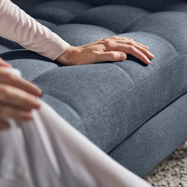 Person som testar komforten i en grå stoppad soffa och känner de mjuka kuddarna.