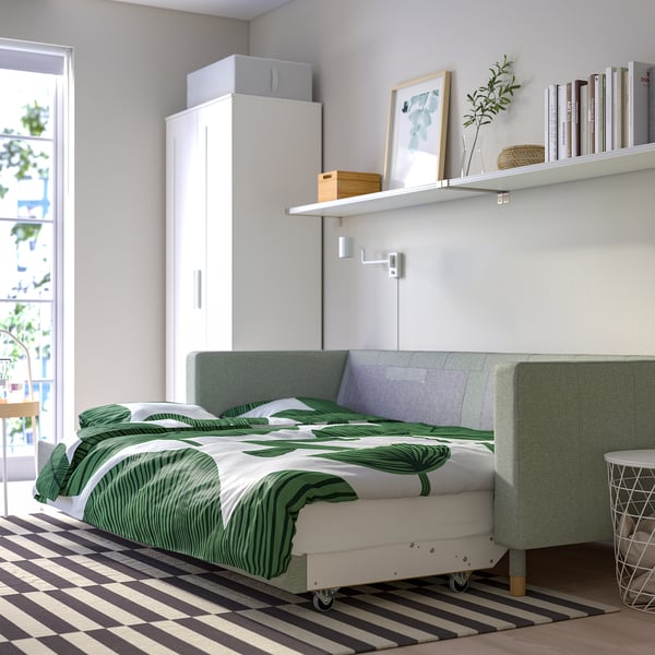Modernt sovrum med bäddsoffa, gröna sängkläder, bokhyllor, matta, garderob, balkongdörr