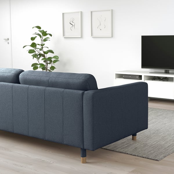 Blå soffa med armstöd vetter mot tv, med avtagbar design. Växt på toppen, mysig miljö.