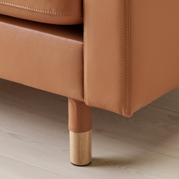 Bruna lädersoffor sidodetalj, som visar tjocka sömmar, slät struktur och träben med guldfinish.