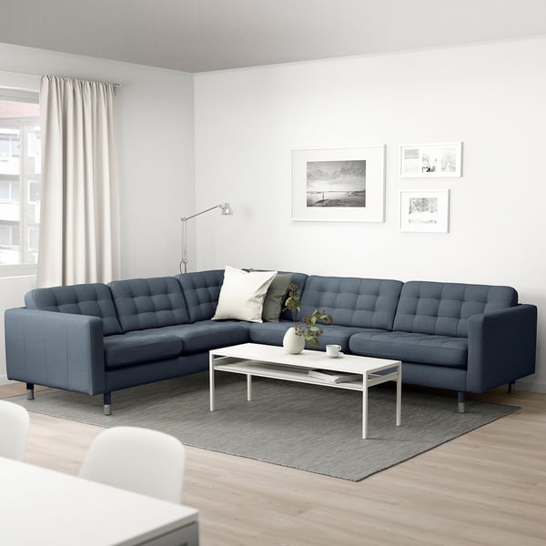 Modernt vardagsrum med en blå l-formad soffa, vitt soffbord och golvlampa.