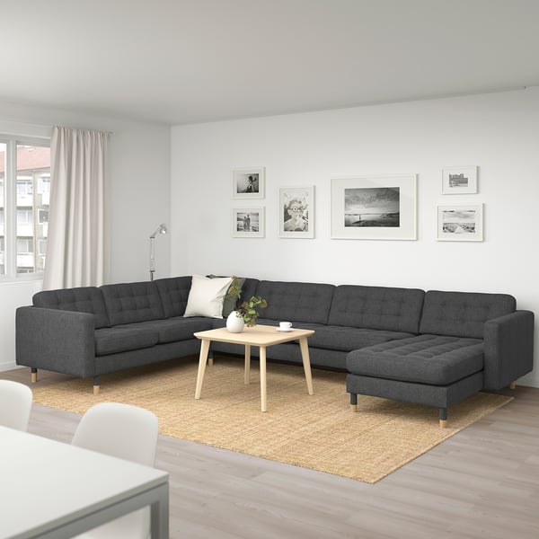 Stor grå l-formad soffa LANDSKRONA, soffbord i trä, matta, vit gardin, väggdekorationer i modernt vardagsrum.
