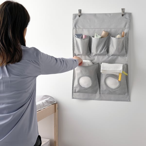 Kvinna som använder grå väggorganisatör för babyartiklar.