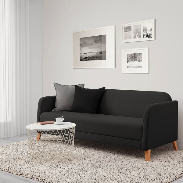 Modernt minimalistiskt vardagsrum med svart LINANÄS soffa, vitt sidobord och svartvit inredning.
