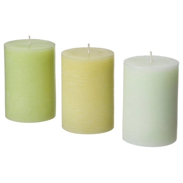 Tre cylindriska ljus i nyanser av grönt, grädde och vitt, var och en med en veke i toppen, arrangerade i en rad.