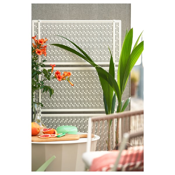 Vit insynsskydd med galler, stål och plast, perfekt för trädgård eller terrass, med blommor till vänster, växt till höger.
